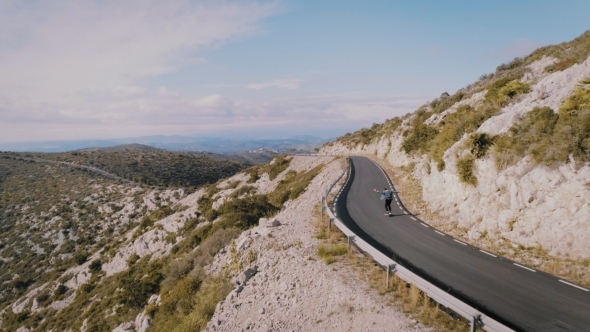 Hipster Man Rides on Skateboard on Mountain Road