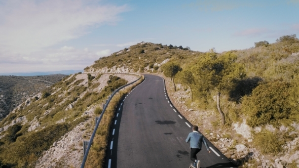 Hipster Man Rides on Skateboard on Mountain Road