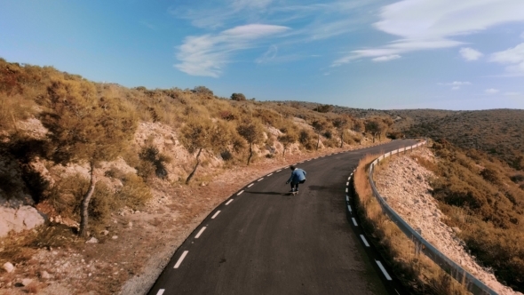 Hipster Man Rides on Skateboard on Mountain Road