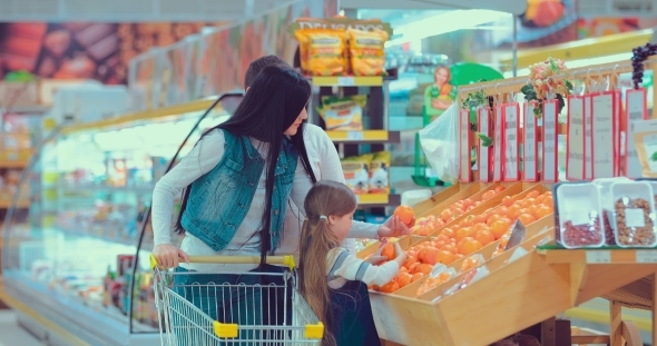 Father, Mother and Little Daughter Choosing Fruits in Supermarket. Mom, Dad and Girl Selecting