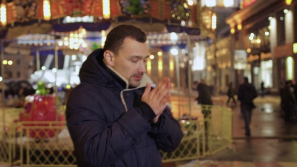 Young Man Tries To Warm Up Outdoors Blowing a Warm Air on His Hands