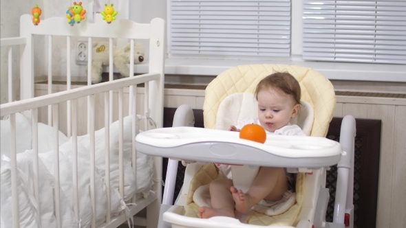 Baby with Tangerine Is Sitting at Table