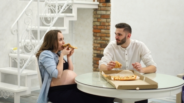 Man and Pregnant Woman Eating Pizza at Home in Their Kitchen