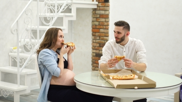 Man and Pregnant Woman Eating Pizza at Home in Their Kitchen A High Fat Meal, Hungry