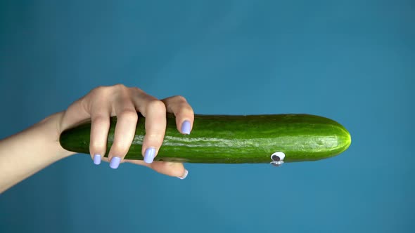 Cucumber with Eyes in a Woman Hand Close Up. Cucumber Looks Around on a Blue Background. Vertical