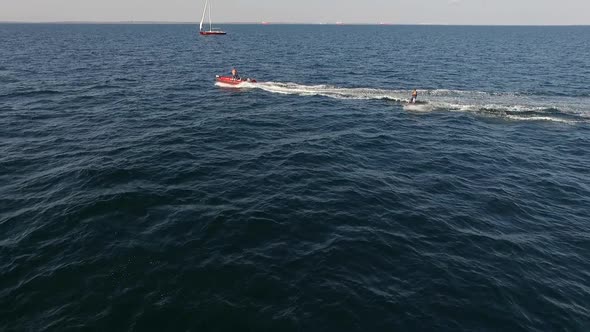 Red Inflatable Boat with Motor and Man on It Pulling Another Male on Board in Sea in Slowmotion