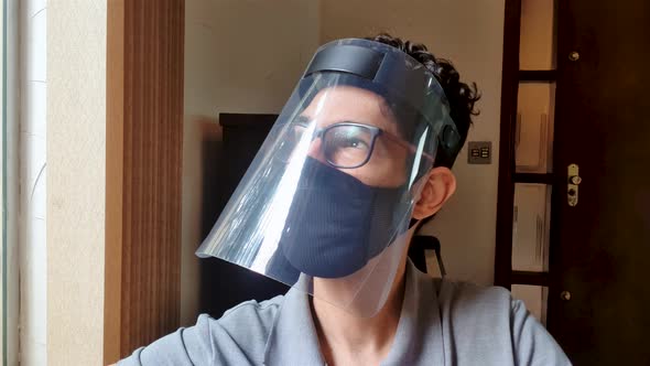 Latin young man wearing covid-19 mask and face shield mask is sitting and slowlying his head to the