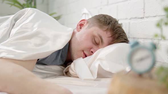 Man Sleeps in Bed with Clock in Foreground