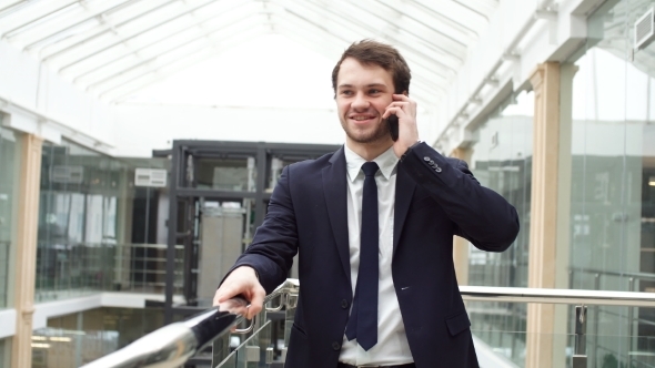 Smiling Modern Young Businessman Speaking on the Phone While Walking.