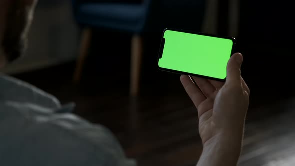 Man at Home Lying on a Couch using Smartphone with Green Mock-up Screen, Doing Swiping, Scrolling