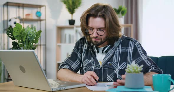 Man in Glasses Sitting at His Workplace at Home and Distantly Working with Papers