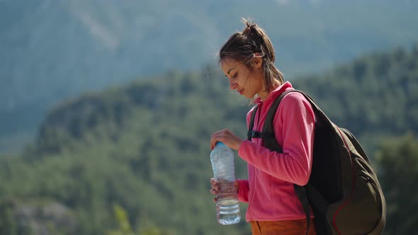 Woman Hiker is Thirsty and Drinks Water From a Plastic Bottle at During Hike in Mountains at Sunny