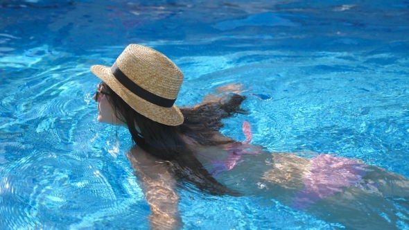 Young Beautiful Girl in Sunglasses and Hat Swimming in Pool. Woman Relaxing in Clear Warm Water on