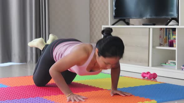 Slim young asian woman is working out on a floor, doing push-up exercise in her living room.