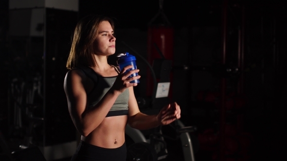 Gorgeous Young Woman with a Towel on Her Neck Drinking Water From a Bottle at the Gym