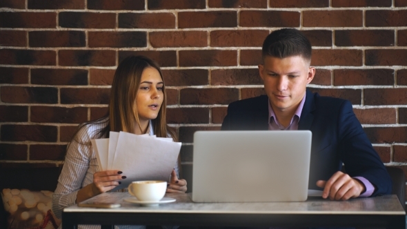 Businessman and a Colleague Discussing Work with Laptop in Cafe