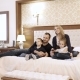 a Happy Family Watching Television in Hotel Room Sitting on Bed - VideoHive Item for Sale