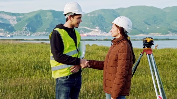 Male and Female Surveyors in Working Uniform and Helmets Smiling Shake Hands After the Deal Ends