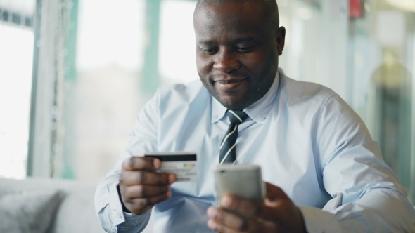 Cheery African American Businessman in Formal Clothes Paying Online Bill Keeping Credit Card.