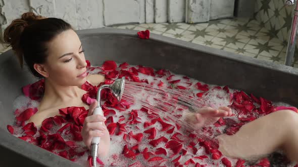 Girl Lies in a Stone Bath with Foam and Petals Washes Herself