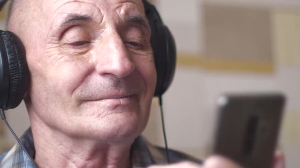 Portrait of a caucasian elderly man in headphones using a smartphone, an active user of social netwo