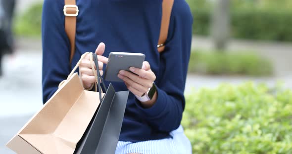 Woman use of mobile phone at outdoor and holding paper bag