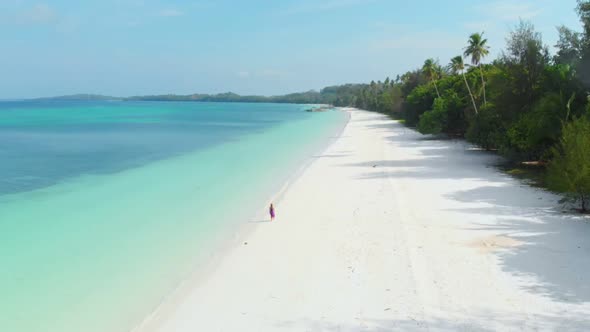 Aerial Slow motion: woman walking on white sand beach turquoise water tropical coastline alt