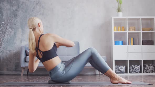 Young and sporty girl in sportswear is doing exercises in home interior.