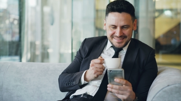 Happy Caucasian Businessman in Formal Clothes Smiling and Looking at His Smartphone Screen.