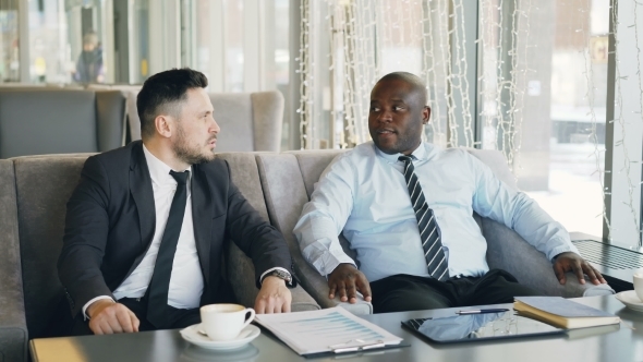 Two Multi-ethnic Businessmen Discussing Startup Ideas in Glassy Cafe During Lunch Time. Coffee Cup