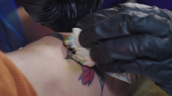 The Tattoo Artist at Work. A Girl Holding a Machine and Applied in Colorful Picture on Skin