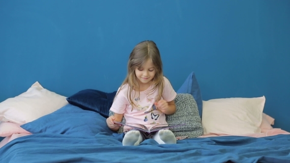 A Little Girl Is Reading a Book on the Bed.
