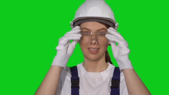 Woman Builder in Blue Overalls and White Hard Hat Put on Protective Glasses