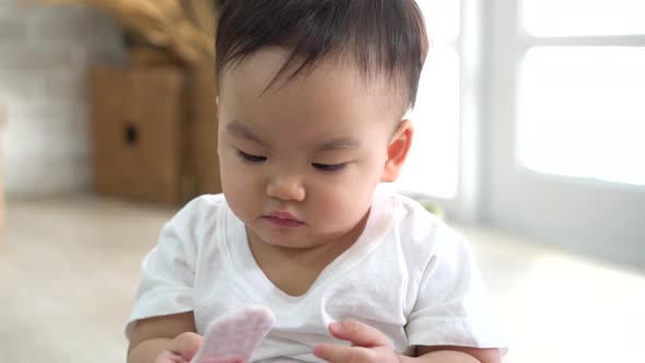 Cute Asian Baby Biting Piece of Snack While Sitting on Floor in Cozy Room at Home