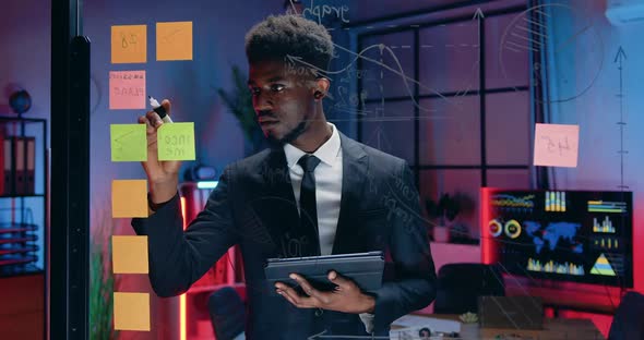 Businessman Writing Remiders on Sticky Notes while Working Over Business Strategy on Glass Board