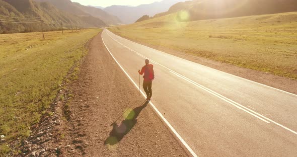 Flight Over Hitchhiker Tourist Walking on Asphalt Road. Huge Rural Valley at Summer Day. Backpack