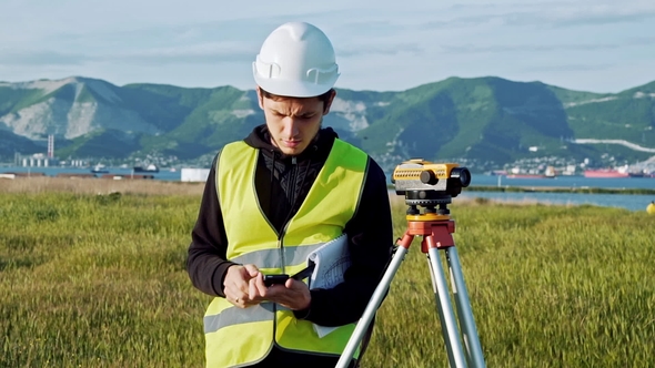 Surveyor Man in Green Work Clothes and Helmet Adjusts the Equipment, Produces Calculations and