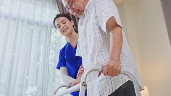 Asian Senior elderly disabled man patient walking slowly with support from nurse at nursing home.