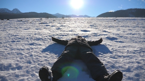 Young Guy Lying on Snow Field and Making Angel on Sunny Day Happy Man Playing and Smiling on Snowy