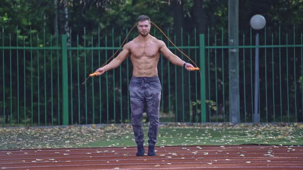 Fit man jumping rope on stadium. Male athlete performs exercise jump on rope on stadium