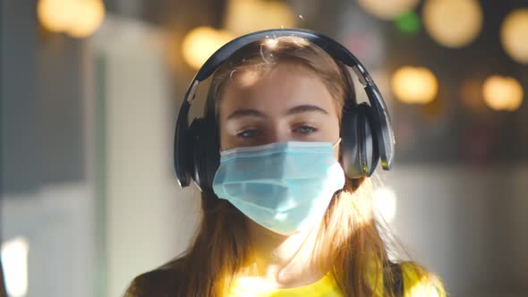 Cute Schoolgirl in Headphones and Safety Mask Walking in School Corridor