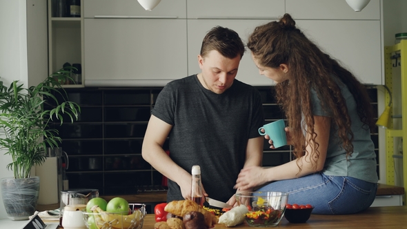Happy Young Couple Cooking and Chatting Happily While Man Cutting Vegetables for Breakfast in the