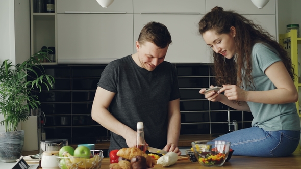 Attractive Young Couple Cooking and Chatting Happily in the Kitchen at Home. Man Cutting Vegetables