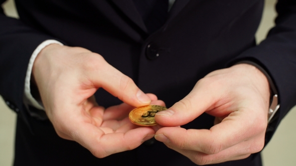 Golden Bitcoin in Hand with Businessman Blurred on Background.