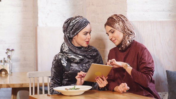 Female Muslim College Students Using Tablet Computer in Cafe.