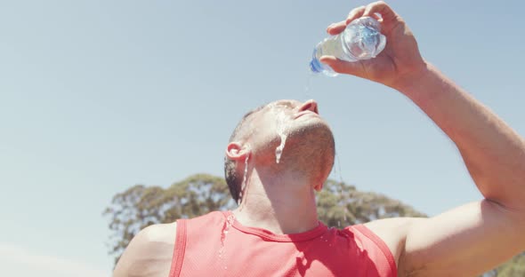 Fit caucasian man pouring water over head, cooling off after exercising in sun