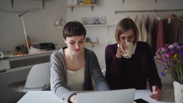 Two Business Woman Working on Notebook on Background Hanging Clothes