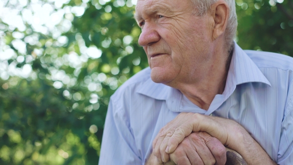Thoughtful Sad Senior Looks at Camera and Tilts Head on Hands in Garden