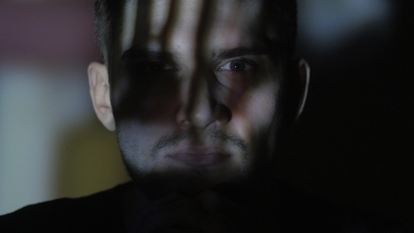 of a Young Man Watching a Video or Film on TV or a Computer Monitor. Reflection on His Face