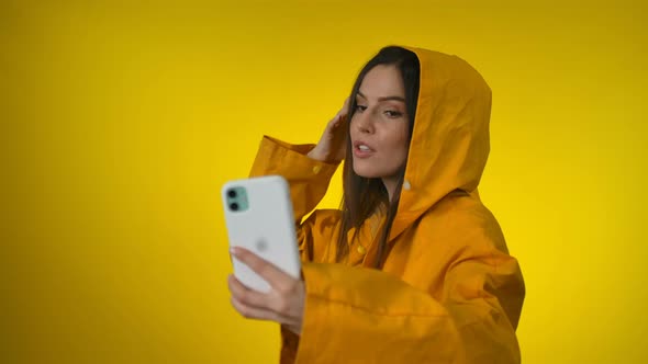 A Young Beautiful Woman in a Bright Yellow Raincoat Makes a Selfie in the Studio